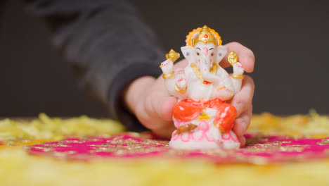 Hand,-Die-Die-Statue-Von-Ganesh-Auf-Den-Tisch-Legt,-Der-Für-Das-Fest-Von-Diwali-1-Geschmückt-Ist