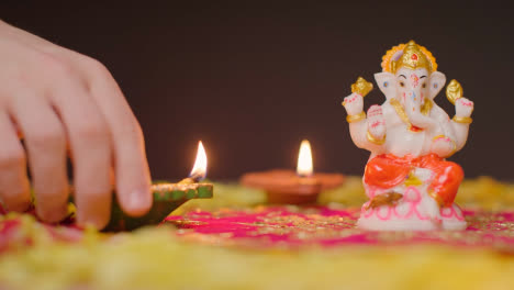 Hand-Arranging-Diya-Lamps-Around-Statue-Of-Ganesh-On-Table-Decorated-For-Celebrating-Festival-Of-Diwali