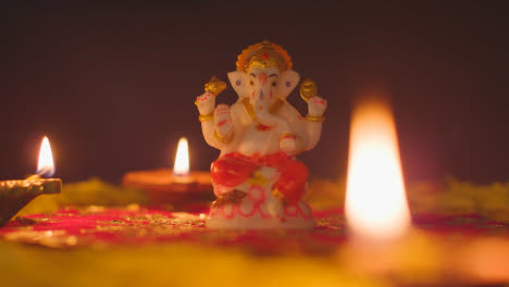 Hand-Arranging-Diya-Lamps-Around-Statue-Of-Ganesh-On-Table-Decorated-For-Celebrating-Festival-Of-Diwali-1