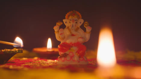 Hand-Lighting-Diya-Lamps-Around-Statue-Of-Ganesh-On-Table-Decorated-For-Celebrating-Festival-Of-Diwali