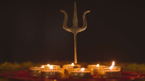 Trishula-Statue-Aus-Metall,-Göttliches-Dreizacksymbol-Des-Hinduismus,-Auf-Dekoriertem-Tisch-Mit-Teelichtern