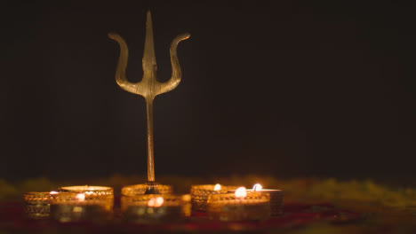 Trishula-Statue-Aus-Metall,-Göttliches-Dreizacksymbol-Des-Hinduismus,-Auf-Geschmücktem-Tisch-Mit-Teelichtern-1