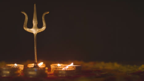 Trishula-Statue-Aus-Metall,-Göttliches-Dreizack-Symbol-Des-Hinduismus,-Auf-Dekoriertem-Tisch-Mit-Ausgeblasenen-Teelichtern