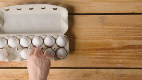 Fotografía-Cenital-De-La-Persona-Que-Elige-De-Una-Caja-De-Doce-Huevos-Abierta-Sobre-Una-Mesa-De-Madera