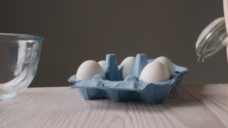 Foto-De-Estudio-De-Ingredientes-Para-Hornear-Y-Utensilios-En-La-Encimera-De-La-Cocina-Con-Una-Persona-Recogiendo-Huevos-4
