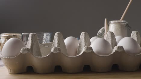 Foto-De-Estudio-De-Ingredientes-Y-Utensilios-Para-Hornear-En-La-Encimera-De-La-Cocina-Con-Una-Persona-Rompiendo-El-Huevo-En-Un-Tazón