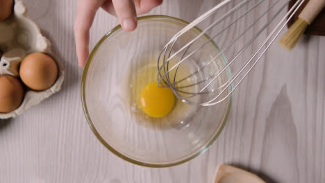 Overhead-Shot-Of-Kitchen-Utensils-On-Kitchen-Worktop-With-Person-Whisking-Egg-In-Glass-Bowl