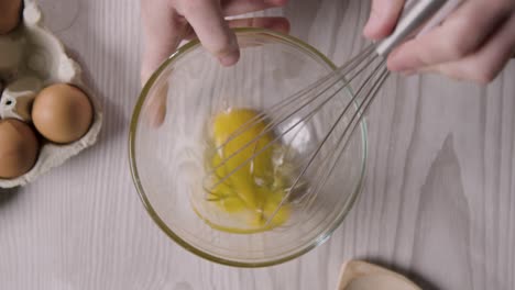Fotografía-Cenital-De-Utensilios-De-Cocina-En-La-Encimera-De-La-Cocina-Con-Una-Persona-Batiendo-El-Huevo-En-Un-Recipiente-De-Vidrio