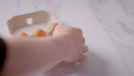 Person-Picking-Up-Box-Of-Brown-Eggs-On-Marble-Work-Surface-Background-1