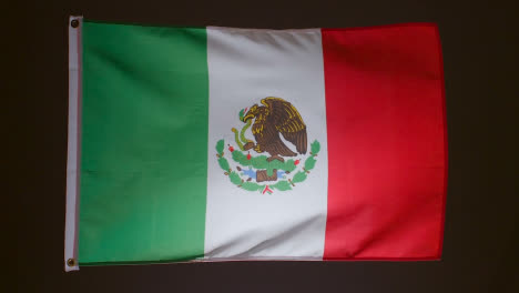 Studio-Shot-Of-Flag-Of-Mexico-Flying-Against-Black-Background