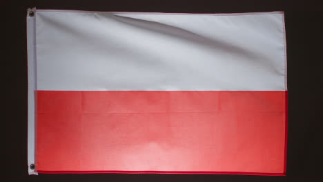 Studioaufnahme-Der-Polnischen-Flagge,-Die-Vor-Schwarzem-Hintergrund-Herunterfällt