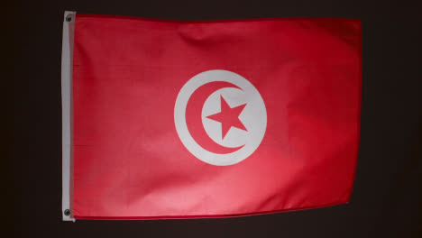 Studio-Shot-Of-Flag-Of-Tunisia-Flying-Against-Black-Background