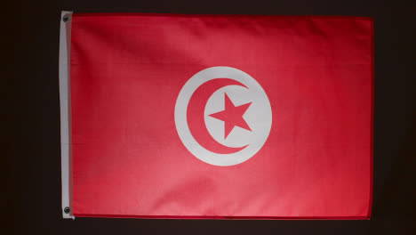 Studio-Shot-Of-Flag-Of-Tunisia-Falling-Down-Against-Black-Background