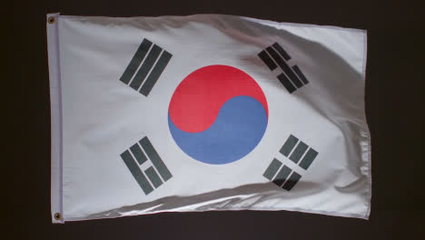 Studio-Shot-Of-Flag-Of-South-Korea-Flying-Against-Black-Background