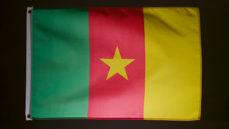 Studio-Shot-Of-Flag-Of-Cameroon-Falling-Down-Against-Black-Background