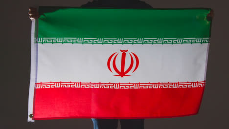 Studioaufnahme-Einer-Anonymen-Person-Oder-Eines-Sportfans,-Der-Die-Flagge-Des-Iran-Vor-Schwarzem-Hintergrund-Hält