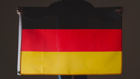 Studioaufnahme-Einer-Anonymen-Person-Oder-Eines-Sportfans,-Der-Die-Flagge-Deutschlands-Vor-Schwarzem-Hintergrund-Hält