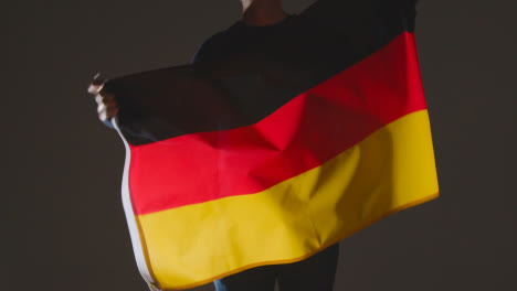 Studioaufnahme-Einer-Anonymen-Person-Oder-Eines-Sportfans,-Die-Die-Flagge-Deutschlands-Vor-Schwarzem-Hintergrund-Schwenken