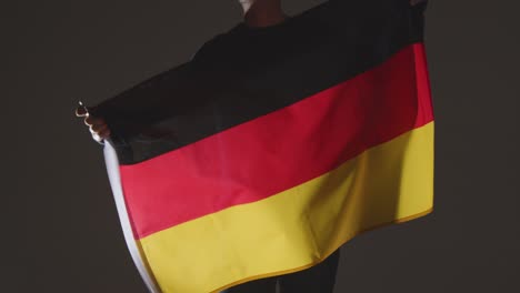 Studio-Shot-Of-Anonymous-Person-Or-Sports-Fan-Waving-Flag-Of-Germany-Against-Black-Background