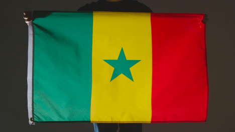 Studioaufnahme-Einer-Anonymen-Person-Oder-Eines-Sportfans,-Der-Die-Flagge-Senegals-Vor-Schwarzem-Hintergrund-Hält