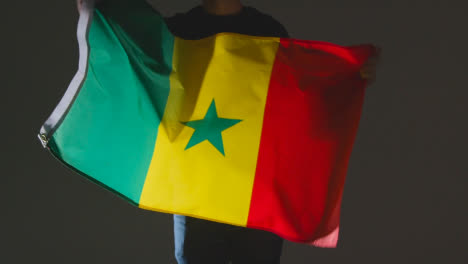 Studioaufnahme-Einer-Anonymen-Person-Oder-Eines-Sportfans,-Die-Die-Flagge-Senegals-Vor-Schwarzem-Hintergrund-Schwenken