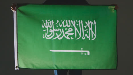 Studio-Shot-Of-Anonymous-Person-Or-Sports-Fan-Holding-Flag-Of-Saudi-Arabia-Against-Black-Background