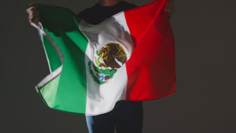 Foto-De-Estudio-De-Una-Persona-Anónima-O-Fanático-De-Los-Deportes-Ondeando-La-Bandera-De-México-Contra-El-Fondo-Negro