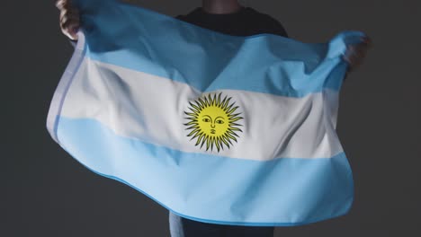 Studio-Shot-Of-Anonymous-Person-Or-Sports-Fan-Waving-Flag-Of-Argentina-Against-Black-Background