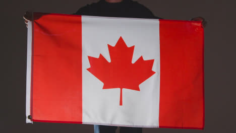 Studioaufnahme-Einer-Anonymen-Person-Oder-Eines-Sportfans,-Der-Die-Flagge-Kanadas-Vor-Schwarzem-Hintergrund-Hält