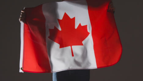 Studioaufnahme-Einer-Anonymen-Person-Oder-Eines-Sportfans,-Der-Die-Flagge-Kanadas-Vor-Schwarzem-Hintergrund-Schwenkt