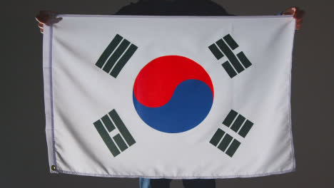 Studioaufnahme-Einer-Anonymen-Person-Oder-Eines-Sportfans,-Der-Die-Flagge-Südkoreas-Vor-Schwarzem-Hintergrund-Hält