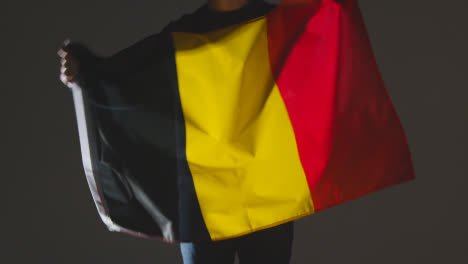 Studioaufnahme-Einer-Anonymen-Person-Oder-Eines-Sportfans,-Der-Die-Flagge-Belgiens-Vor-Schwarzem-Hintergrund-Schwenkt