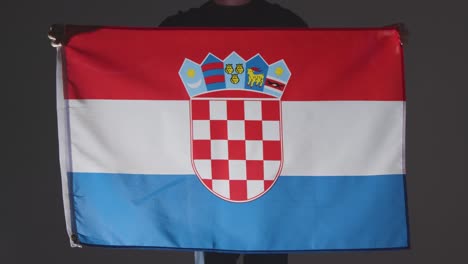 Foto-De-Estudio-De-Una-Persona-Anónima-O-Fanático-De-Los-Deportes-Que-Sostiene-La-Bandera-De-Croacia-Contra-Fondo-Negro