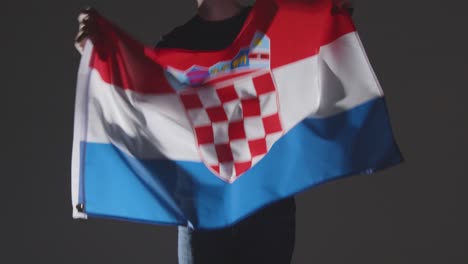 Foto-De-Estudio-De-Una-Persona-Anónima-O-Fanático-De-Los-Deportes-Ondeando-La-Bandera-De-Croacia-Contra-Fondo-Negro