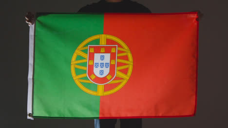 Studioaufnahme-Einer-Anonymen-Person-Oder-Eines-Sportfans,-Der-Die-Flagge-Portugals-Vor-Schwarzem-Hintergrund-Hält