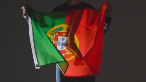 Studioaufnahme-Einer-Anonymen-Person-Oder-Eines-Sportfans,-Die-Die-Flagge-Portugals-Vor-Schwarzem-Hintergrund-Schwenken
