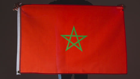 Studioaufnahme-Einer-Anonymen-Person-Oder-Eines-Sportfans,-Der-Die-Marokkanische-Flagge-Vor-Schwarzem-Hintergrund-Hält