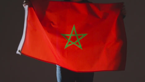 Studioaufnahme-Einer-Anonymen-Person-Oder-Eines-Sportfans,-Der-Die-Flagge-Marokkos-Vor-Schwarzem-Hintergrund-Schwenkt