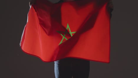 Studio-Shot-Of-Anonymous-Person-Or-Sports-Fan-Waving-Flag-Of-Morocco-Against-Black-Background