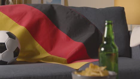 Flag-Of-Germany-Draped-Over-Sofa-At-Home-With-Football-Ready-For-Match-On-TV-1