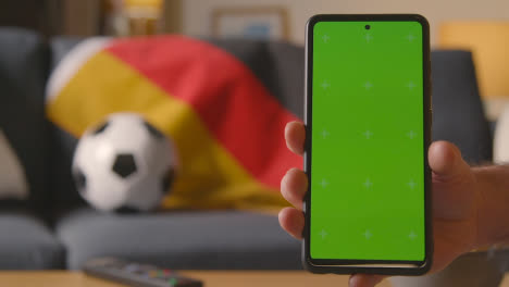 Green-Screen-Mobile-Phone-With-German-Flag-Draped-Over-Sofa-At-Home-Ready-For-Soccer-Match