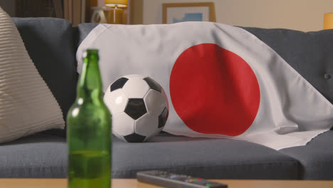 Flagge-Von-Japan-Drapiert-über-Sofa-Zu-Hause-Mit-Fußball-Bereit-Für-Spiel-Im-Fernsehen