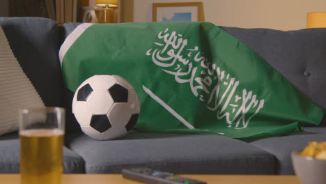 Flag-Of-Saudi-Arabia-Draped-Over-Sofa-At-Home-Ready-For-Match-On-TV