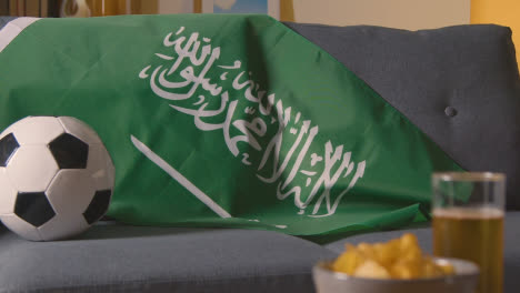 Flag-Of-Saudi-Arabia-Draped-Over-Sofa-At-Home-Ready-For-Match-On-TV-1
