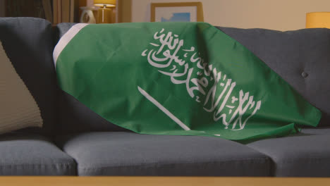 Flag-Of-Saudi-Arabia-Draped-Over-Sofa-At-Home-Ready-For-Match-On-TV-2
