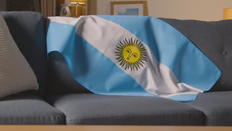 Flag-Of-Argentina-Draped-Over-Sofa-At-Home-With-Football-Ready-For-Match-On-TV