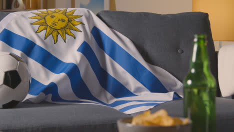 Flagge-Von-Uruguay-über-Dem-Sofa-Zu-Hause-Mit-Fußball-Bereit-Für-Das-Spiel-Im-Tv-1