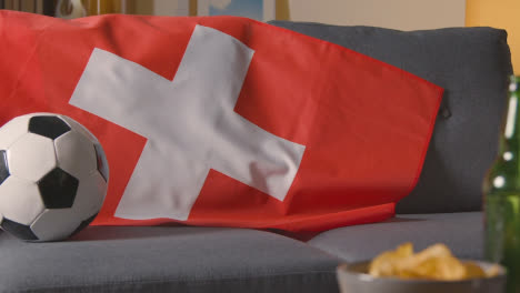 Flag-Of-Switzerland-Draped-Over-Sofa-At-Home-With-Football-Ready-For-Match-On-TV-1