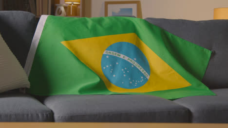 Flag-Of-Brazil-Draped-Over-Sofa-At-Home-Ready-For-Match-On-TV