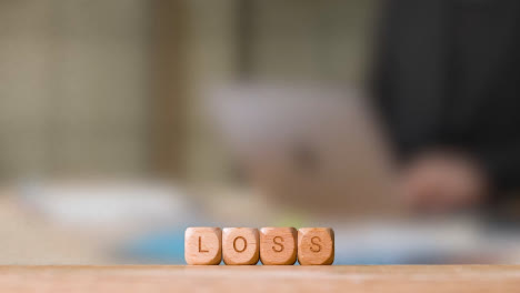 Concepto-De-Negocio-Cubos-De-Letras-De-Madera-O-Pérdida-De-Ortografía-De-Dados-Con-Una-Persona-De-Oficina-Que-Trabaja-En-Una-Computadora-Portátil-En-Segundo-Plano